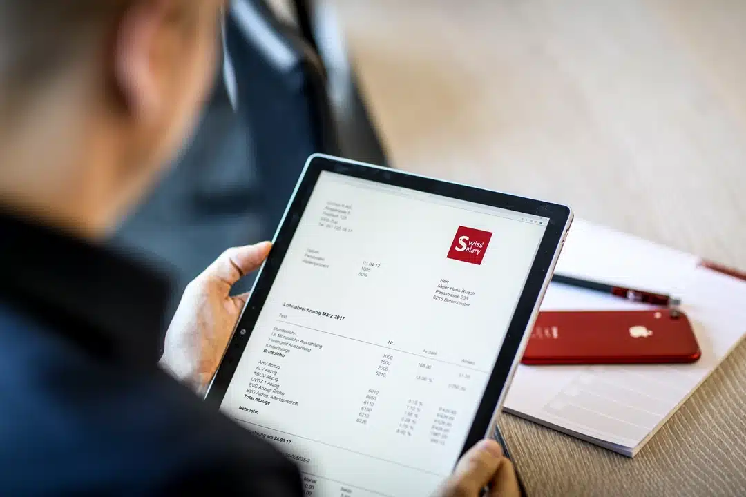 Person hält ein Tablet mit einer digitalen SwissSalary-Lohnabrechnung, die die papierlose Lohnabrechnung hervorhebt.